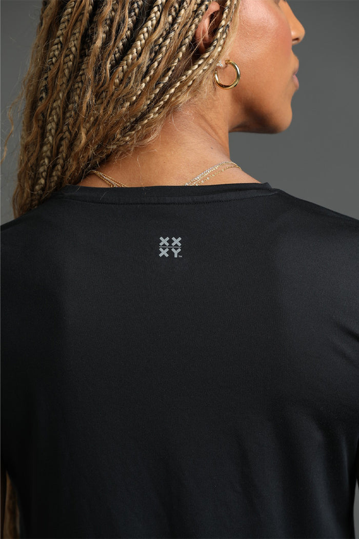 Person wearing a black shirt with a small logo on the back against a gray background || black