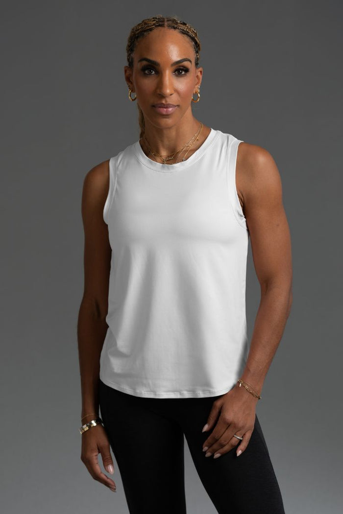 Woman wearing a white sleeveless top and black leggings against a gray background || White
