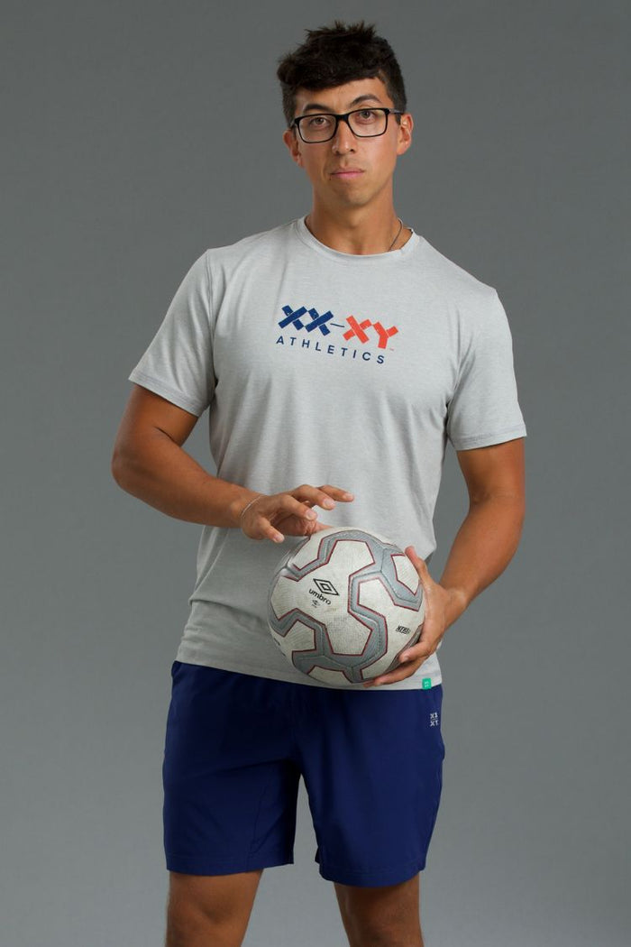 Person wearing a gray 'XXXY Athletics' t-shirt holding a soccer ball on a gray background || Black/Dark Heather Gray/Light Heather Gray
