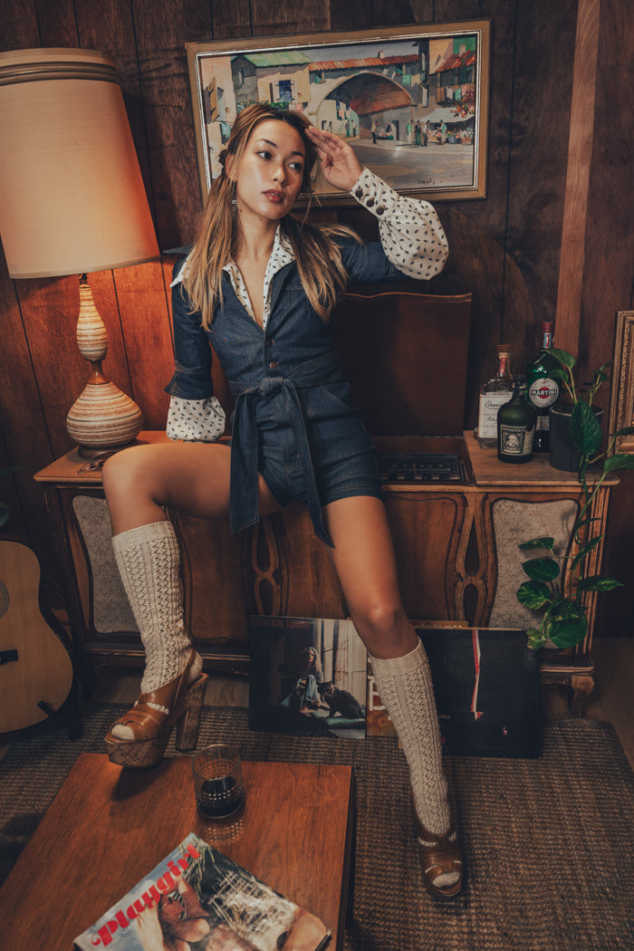 stylish woman in a 1970s romper stands by a record player in a soulful, retro inspired home interior