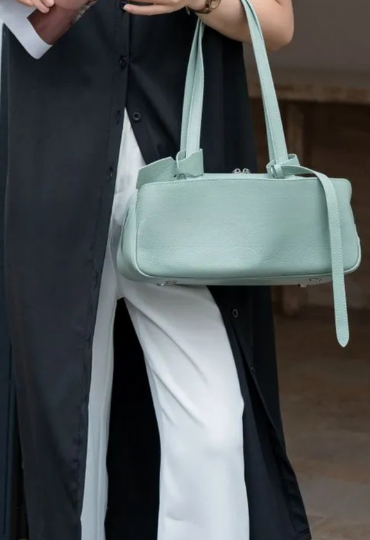 Person holding a light green handbag with a blurred background