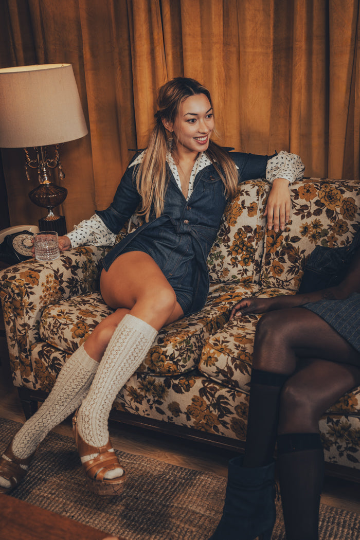 model in a funky 70s romper lounges in a retro home setting with wood - paneled walls and vinyl records